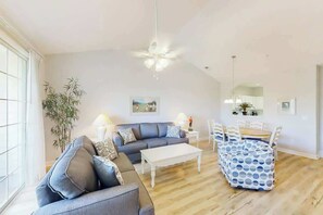 Una sala de estar con sofá, mesa de centro, mesa de comedor, sillas y un ventilador de techo.