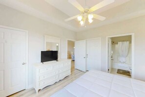 Une chambre à coucher comprenant un lit, une commode, un téléviseur et un ventilateur de plafond.