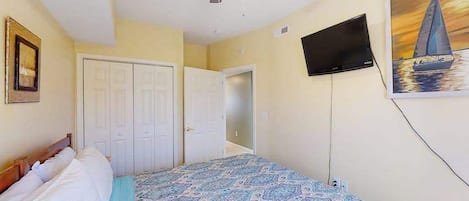 Un dormitorio con cama, ventilador de techo, televisión y un cuadro en la pared.
