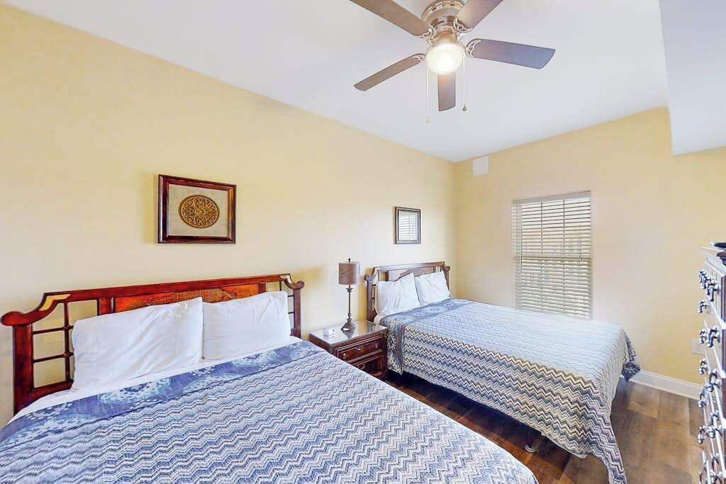 A hotel room with two beds, a ceiling fan, a window with blinds, and a wall-mounted picture.