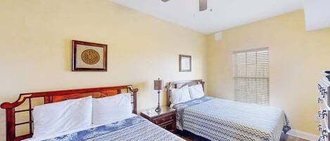 A hotel room with two beds, a ceiling fan, a window with blinds, and a wall-mounted picture.