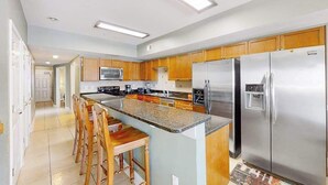 Una cocina moderna con una isla central, electrodomésticos de acero inoxidable, armarios de madera y piso de baldosas.