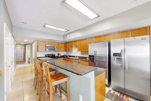 A modern kitchen with a central island, stainless steel appliances, wooden cabinets, and a tiled floor. - Coconut Grove Unit 405 (North Myrtle Beach)