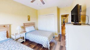 Habitación de hotel con dos camas, ventilador de techo, televisor y un armario blanco.