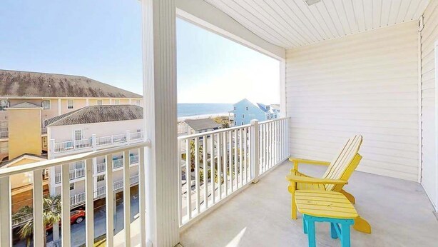 Un balcón con vista a la playa y casas, con dos sillas Adirondack amarillas.