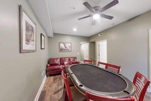 A room with a pool table, red chairs, a ceiling fan, and framed pictures on the wall. - Coconut Grove Unit 405 (North Myrtle Beach)