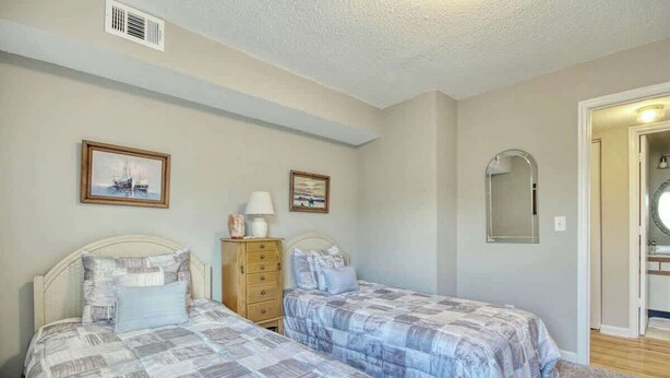 A bedroom with two beds, a dresser, a mirror, and artwork on the wall. - Home Away From Home Unit J (Surfside Beach)