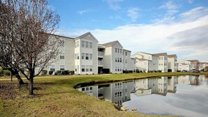 A residential building complex with multiple apartment buildings, a small pond, and a tree. - Home Away From Home Unit J (Surfside Beach)