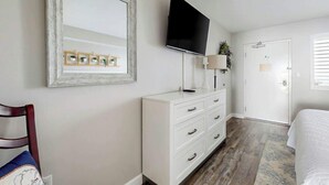Een hotelkamer met een grote spiegel, een flatscreen televisie, een witte dressoir, een bed en een deur met lichtschakelaar.
