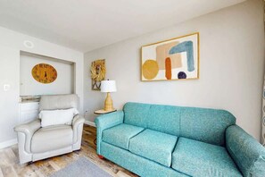Ein Wohnzimmer mit einer Couch, einem Sessel, einer Wanduhr, einer Lampe und einem gerahmten abstrakten Gemälde.
