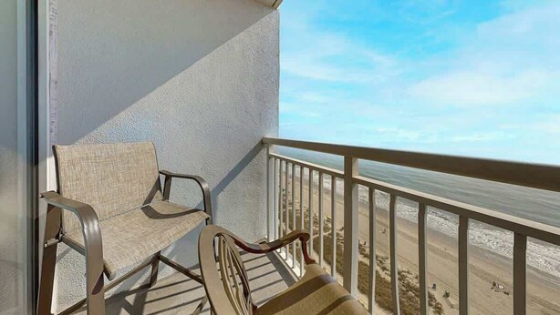 Een balkon met twee stoelen en uitzicht op het strand.
