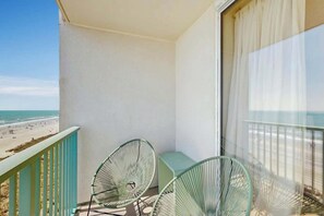 A balcony with two green wire-framed chairs, a light blue table, and a view of the beach. - The Pinnacle Unit 601 (North Myrtle Beach)