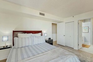 A bedroom with a bed, bedside tables, a wardrobe, and a door leading to another room. - The Pinnacle Unit 601 (North Myrtle Beach)