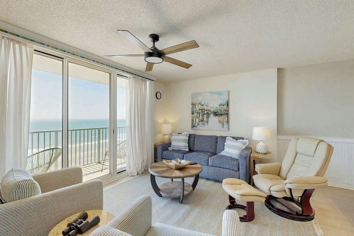 Une chambre d’hôtel avec un balcon, un ventilateur de plafond, un ensemble de canapés, une table basse et un fauteuil.