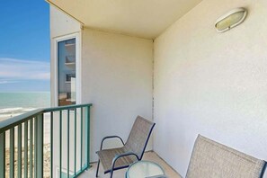 Un balcon avec vue sur la plage, une chaise et une petite table.