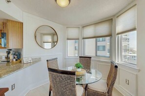 A dining area with wicker chairs, a glass table, and a round mirror on the wall. - The Pinnacle Unit 601 (North Myrtle Beach)