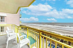 Ein Balkon mit Blick auf den Strand, weißen Plastikstühlen und einem Pool.