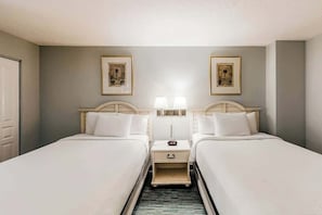 A hotel room with two beds, a nightstand, a lamp, and framed artwork on the wall. - Bay Watch Resort 0411 (North Myrtle Beach)