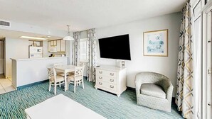 A hotel room with a dining area, a flat-screen TV, a patterned curtain, and a framed picture on the wall. - Bay Watch Resort 0411 (North Myrtle Beach)