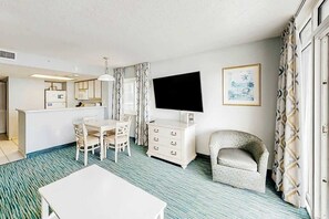 A hotel room with a dining area, a flat-screen TV, a patterned curtain, and a framed picture on the wall. - Bay Watch Resort 0411 (North Myrtle Beach)