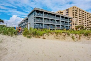 Ein mehrstöckiges Hotel mit Balkonen in der Nähe eines sandigen Strandes mit Vegetation.