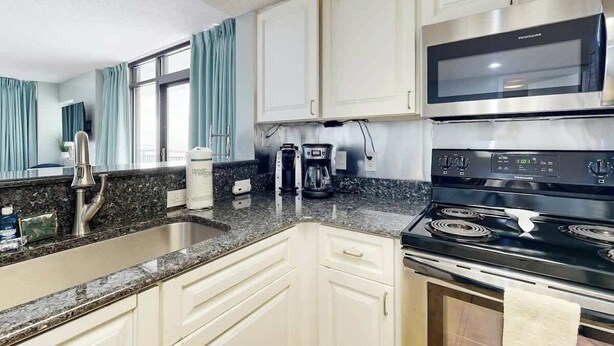 A kitchen with white cabinets, a stainless steel microwave, a stove, and a coffee maker. - Sand Dunes Resort 910 (Myrtle Beach)