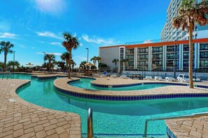 A swimming pool with multiple lanes, surrounded by lounge chairs and palm trees, with a building in the background. - Sand Dunes Resort 910 (Myrtle Beach)