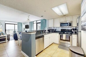 Une cuisine moderne avec des meubles blancs, un îlot central, des appareils électroménagers en acier inoxydable et un coin repas comprenant un canapé et des chaises.