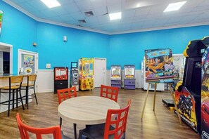 Ein Zimmer mit blauer Wand, Holzboden, einem runden Tisch mit Stühlen und verschiedenen Spielautomaten.