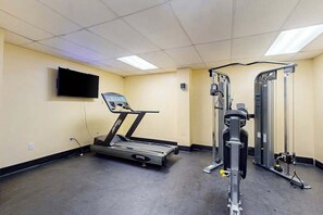 Ein Fitnessstudio mit Laufband, Kraftgeräten und einem an der Wand montierten Fernseher.