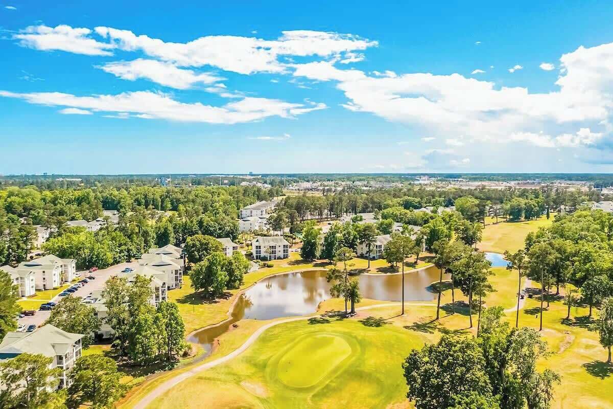 Ein Golfplatz mit Teich, umgeben von Wohnhäusern und Bäumen.