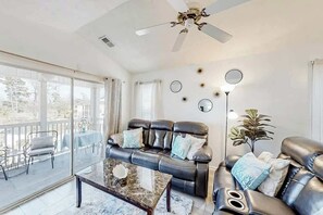 Un salon avec un canapé en cuir, une table basse en verre et un ventilateur de plafond.