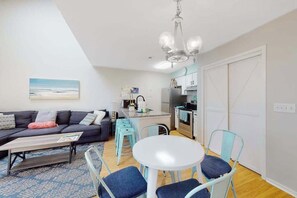 A compact living space with a sofa, coffee table, dining table, and chairs. A kitchen area is visible with a refrigerator, oven, and sink. - Beach Golfer's Nest Retreat (Little River)
