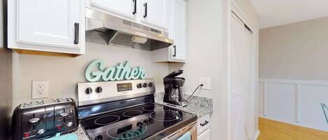 A kitchen with white cabinets, a stove, a toaster, and a coffee maker.