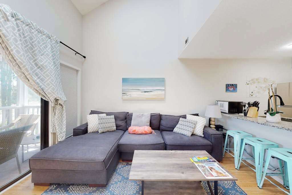 A modern living room with a sectional sofa, a coffee table, and a kitchen area with bar stools.