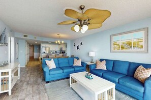 Un salon avec un canapé bleu, une table basse blanche et un ventilateur de plafond.