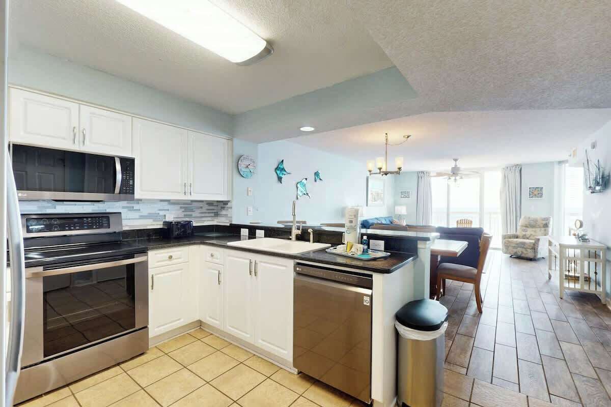 A modern kitchen with white cabinets, stainless steel appliances, and a tiled floor.