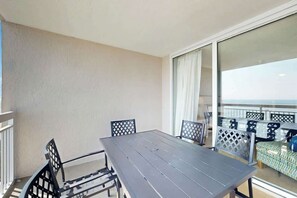 Ein Balkon mit Tisch und Stühlen, Blick auf das Meer und ein gemustertes Sofa.