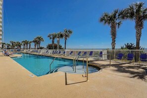 Une piscine dotée d’une terrasse ensoleillée, entourée de palmiers et de chaises longues.