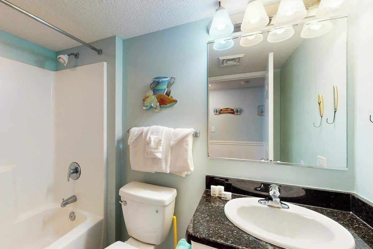 Une salle de bain équipée d’une baignoire, de toilettes, d’un lavabo et d’un miroir au-dessus du lavabo.