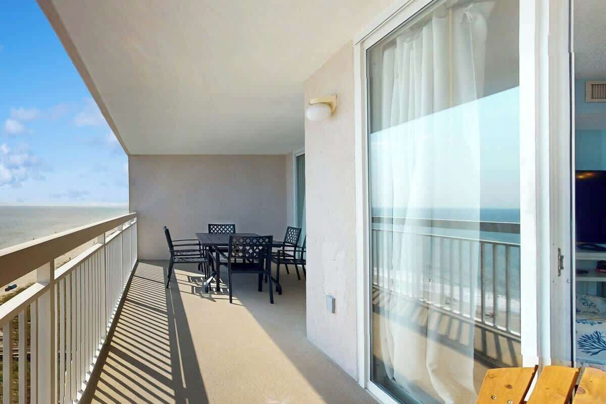 A balcony with a table and chairs, a view of the sea, and a sliding glass door leading to a room.