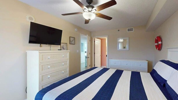 Ein Schlafzimmer mit einem Bett, einem Deckenventilator, einem Fernseher und einer Kommode.