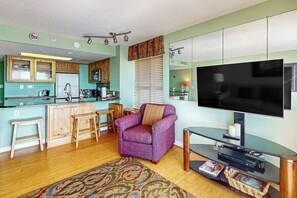A compact living space with a kitchenette, a seating area with a purple armchair, a flat-screen TV, and a wooden dining table. - Bay Watch Resort 0732 (North Myrtle Beach)