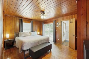 Ein Schlafzimmer mit Holzwänden, einem Bett, Nachttischen, einer Bank, einem Deckenventilator und einer Tür zu einem Außenbereich.