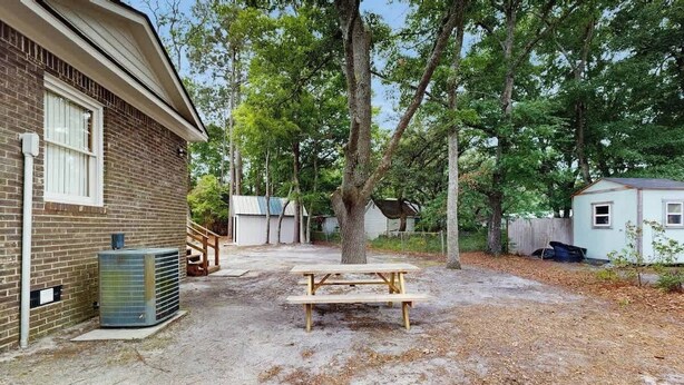 A backyard with a picnic table, a brick house, and trees. - The Little Brick Cottage (Murrells Inlet)