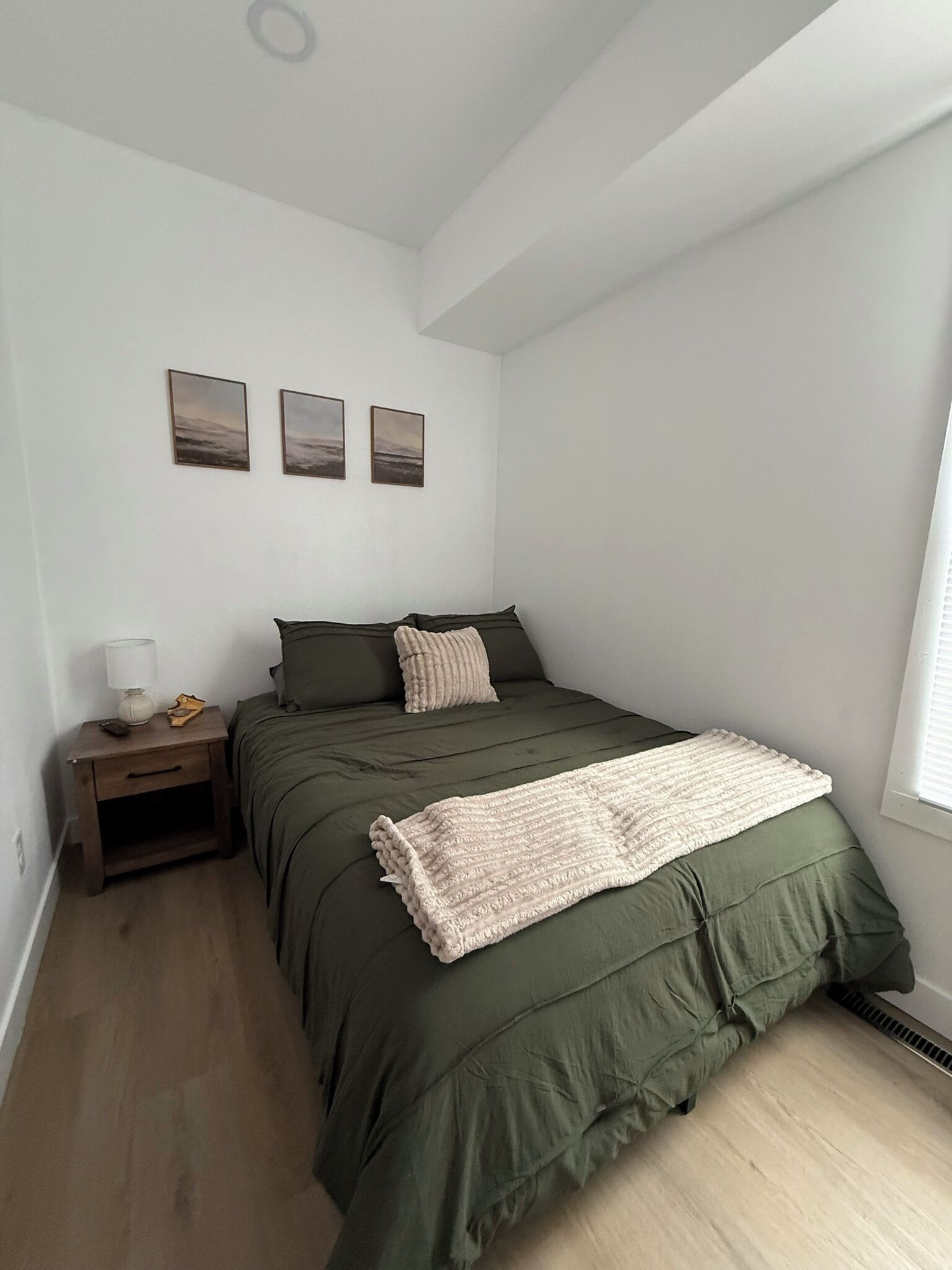 Une chambre à coucher comprenant un lit, une table de chevet, une lampe et trois tableaux accrochés au mur.