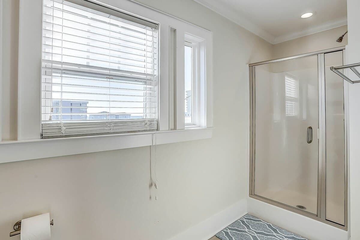 A bathroom with a shower, a toilet, and a window with blinds.