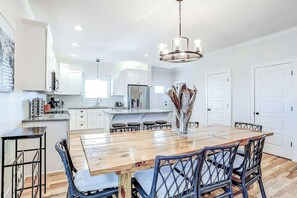 A modern kitchen with white cabinetry, a wooden dining table, and blue chairs. - Strand Ave Estate Retreat (North Myrtle Beach)