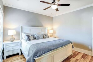 A bedroom with a bed, nightstands, lamps, a ceiling fan, and wooden flooring. - Strand Ave Estate Retreat (North Myrtle Beach)