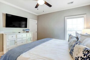Ein Schlafzimmer mit einem Bett, einem Schminktisch, einem Fernseher, einem Deckenventilator und einem Fenster.